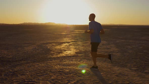 Athletic man working out with battle ropes on a dry lake at sunset