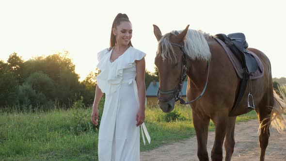 Lady Brunette with Long Hair in Ponytail Wanders with Horse