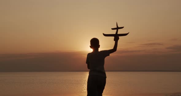 Happy Child Runs with a Toy Airplane on a Sunset Background at the Sea