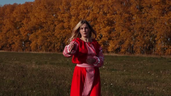Militant Concept on an Autumn Field - Blonde Woman in Red National Dress Training Her Swordplay