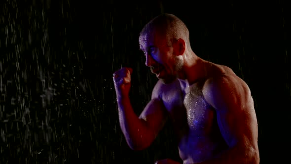 a Muscular Man with a Bare Torso Fights with a Shadow in the Streams of Water on a Dark Background