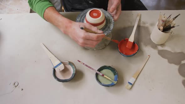 Overhead view of male potter using brush to paint pot on potters wheel at pottery studio