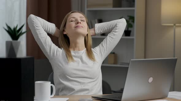 Young good looking caucasian girl stretching and smiling while sitting at the kitchen table