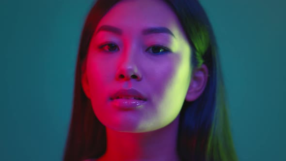 Studio Portrait of Young Millennial Korean Lady Turning to Camera and Smiling Posing in Bright Neon
