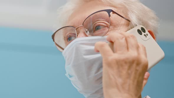 Positive senior lady doctor in disposable mask talks on mobile phone