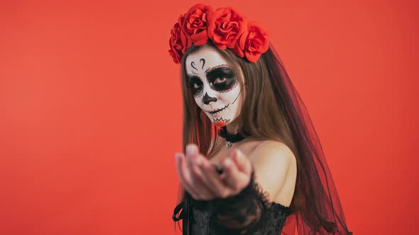 Day of Dead Woman with Sugar Skull Makeup is Turning Sideways Beckoning you By Her Hand Posing on