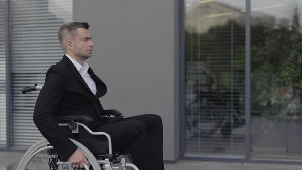 Side View of Businessman in Wheel Chair Looking Ahead While Going at Street