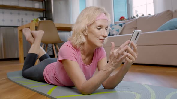 Mature Woman Using Cellphone Lying on Sport Mat at Home