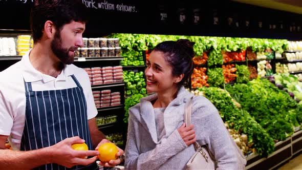 Smiling male staff assisting a woman with grocery shopping