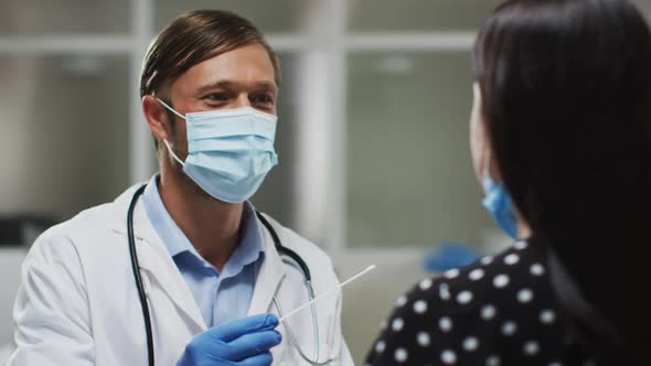 Caucasian male doctor wearing face mask and gloves taking swab test from patient
