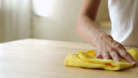 Housewife Wiping Spilled Coffee or Tea From a Wooden Kitchen Table. Female Using a Household Cleaner