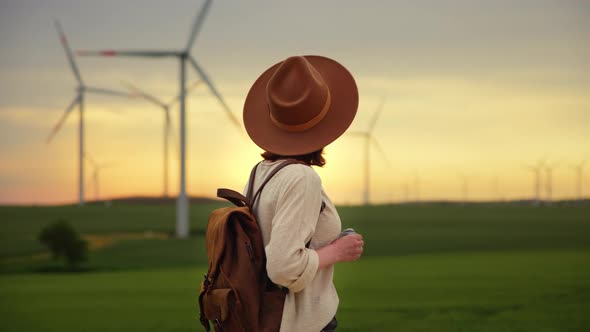 Beautiful girl in a hat with a camera in a field with windmills