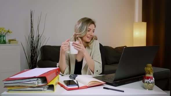 A smiling young woman having coffee break at work on laptop