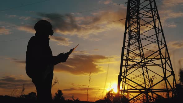 Silhouette of Engineer Standing on Field with Electricity Towers