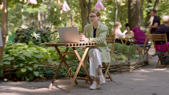 Happy Woman in Headphones Communicating Via Video Call Being in a Conference Sitting Outdoors on