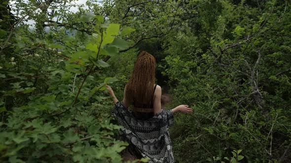 An Attractive Girl with Long Red Hair in Short Shorts and a Summer Cape Walks