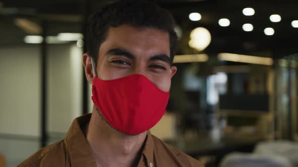 Portrait of a mixed race businessman wearing face mask looking at camera in modern office