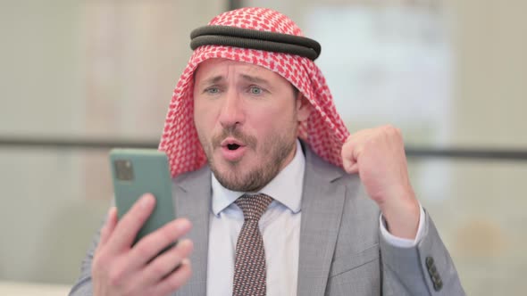 Portrait of Middle Aged Arab Businessman Celebrating on Smartphone