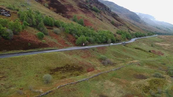 Cinematic panning drone shot scottish highland road winding through a valley