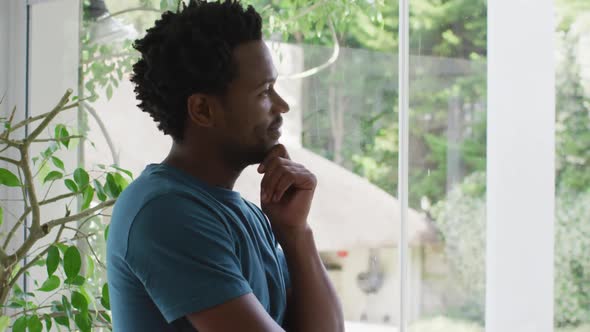 Thoughtful biracial man standing at window and looking into distance