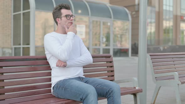 Pensive Young Man Thinking While Sitting Outdoor on Bench