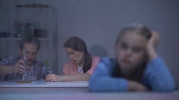 Upset Girl Looking Through Rainy Window Parents Drinking Vodka on Background