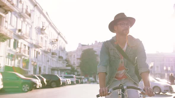 Young Stylish Hipster Man in Hat and Glasses Riding Bike in City Centre on Sunny Day Slow Motion