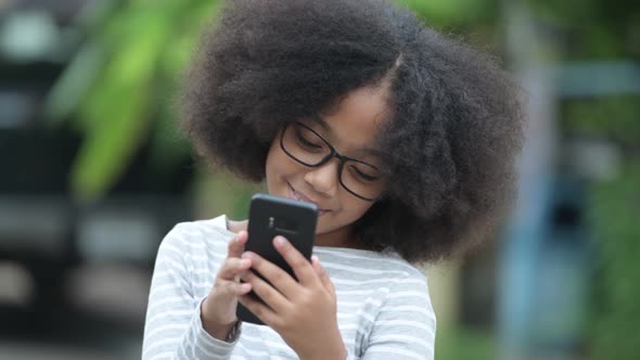 Young Cute African Girl with Afro Hair Using Phone in the Streets Outdoors