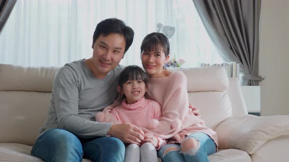 Portrait of Asian happy family sitting on sofa and looking at camera with smile together at home.