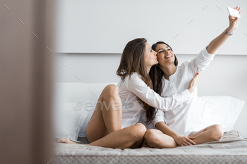  of themselves with a phone in a luxorious bedroom and giving a kiss on cheek