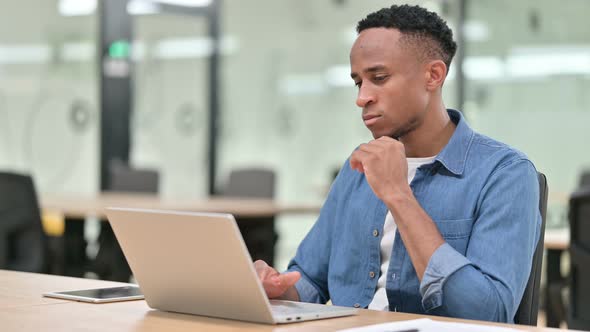 Casual African Man Thinking and Working on Laptop in Office 