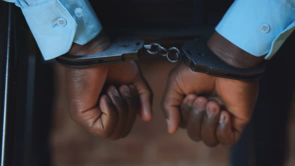 Close Up of Afroamerican Criminal in Handcuffs Shaking Hands Trying To Free