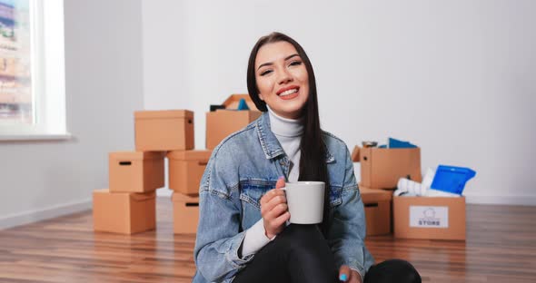 Cheerful Caucasian Woman Sitting on Floor Living Room with Cup of Coffee and Thinking About