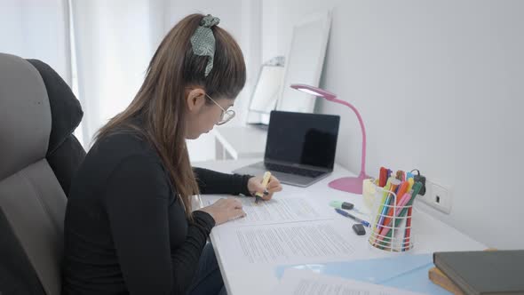 A Young Girl Sitting at a Study Table and Highlighting Her Study Material