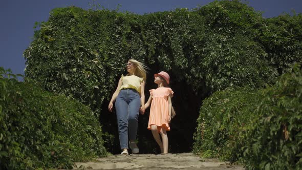 Attractive Blond Mother Walking with Daughter in the Summer Garden or Park Holding Hands