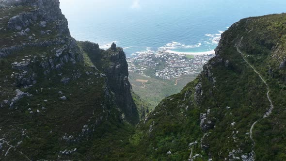Aerial Drone Sot of Beautiful Green Mountain Valley looking Down onto a Sunny Camps Bay Beach in Cap