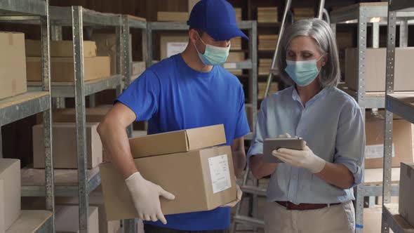 Female Manager and Courier Wearing Face Masks Talking in Warehouse