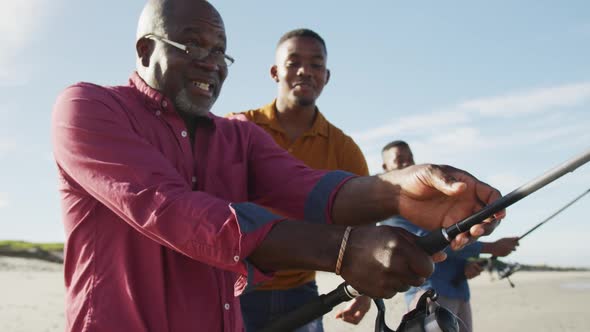 African american senior father and twin teenage sons standing on a beach fishing and talking