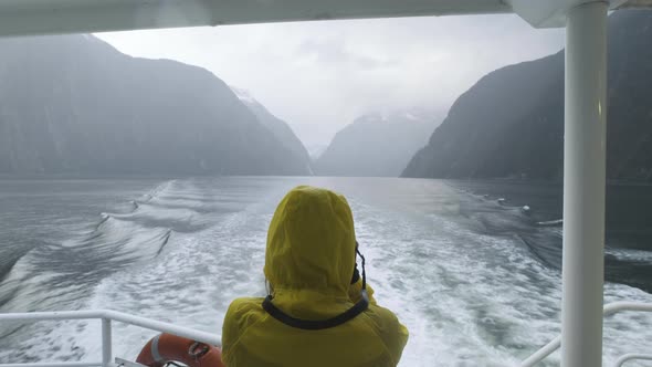 Girl in a bright yellow rain jacket photographing the Fjords of Milford Sound from a boat in New Zea