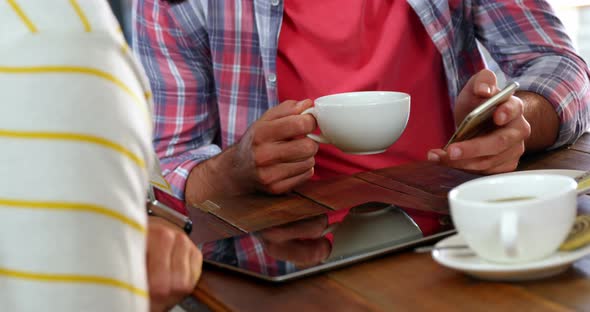 Friends interacting over mobile phone while having coffee