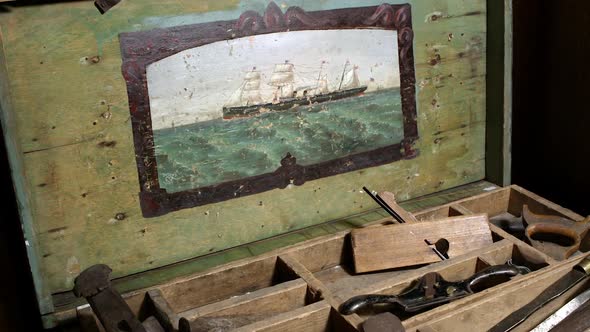 Panning view over old tools in chest with painting of boat