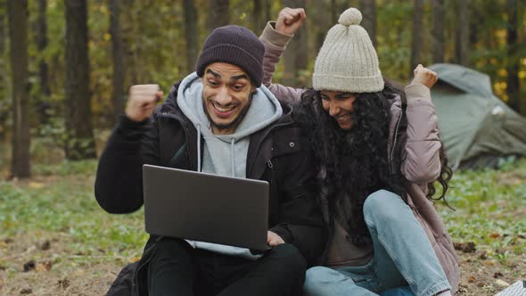 Young Excited Happy Family Couple in Love Sitting in Nature Reading Good News on Laptop Surprised
