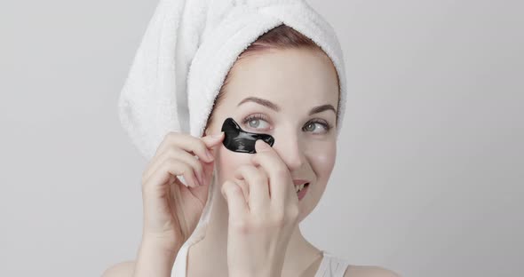 Girl with Towel on Head Applying Black Collagen Pads Posing Isolated on Light Gray Background