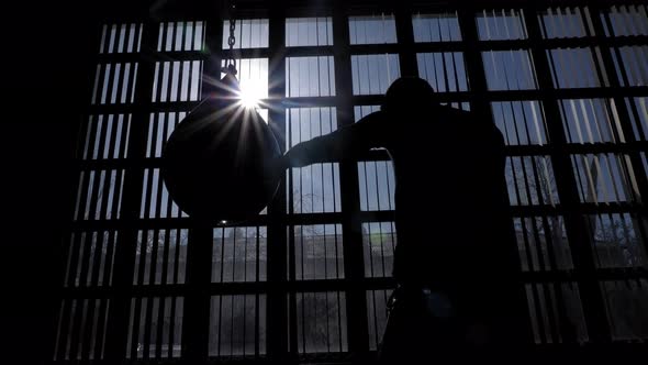 The Silhouette of a Muscular Man Boxing with a Punching Bag in the Gym