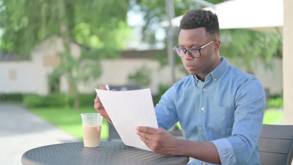 African Man Reading Documents in Outdoor Cafe