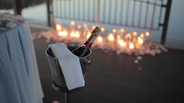 A Bottle of Champagne in an Ice Bucket Against the Background of Burning Candles