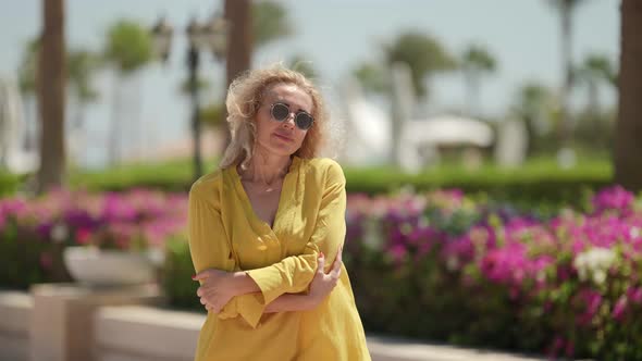 a Curlyhaired Blonde in Sunglasses and a Yellow Dress Poses Against the Background of a Blurred