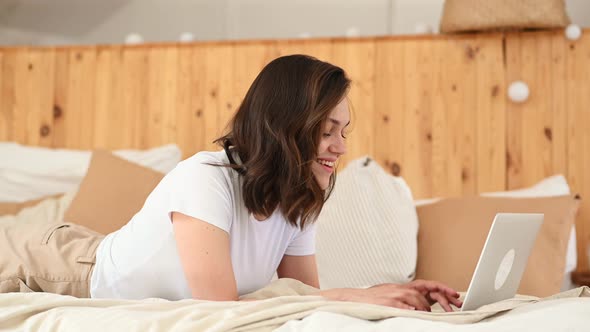 Young Attractive Woman Lying on a Bed in Working on a Laptop