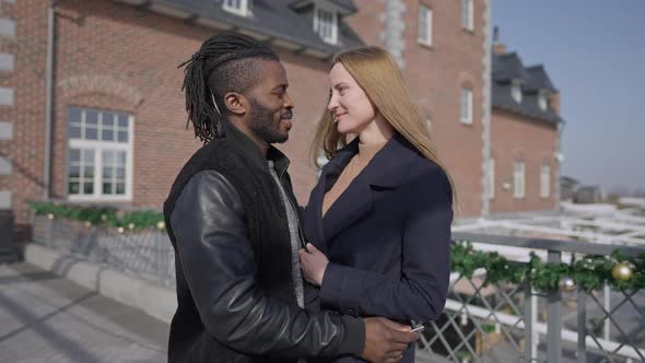 Hugging Interracial Husband and Wife Standing on Sunny Day Outdoors As Man Giving Key From Luxurious