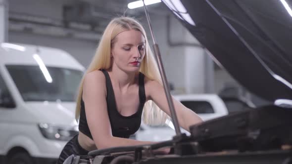 Camera Moving Around Beautiful Blond Caucasian Woman Tightening Screws in Open Car Hood. Female Auto